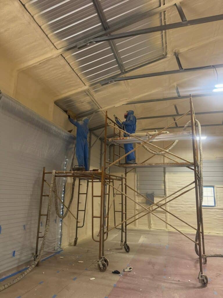 Clark Spray Foam crew on scaffolding spraying foam on a metal building ceiling