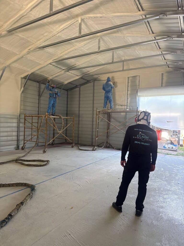 Crew on scaffolding spraying foam insulation in a metal building