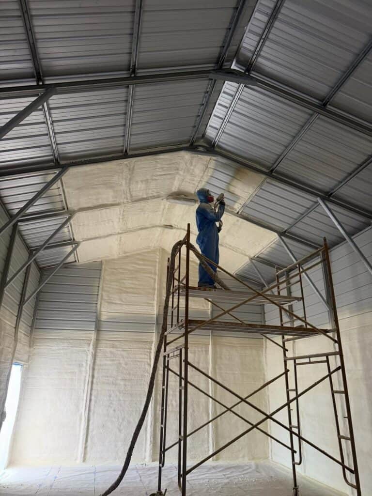 Installer on scaffolding spraying foam on a metal building gable wall